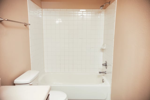 Bathroom with white tiled shower and tub, and a toilet.