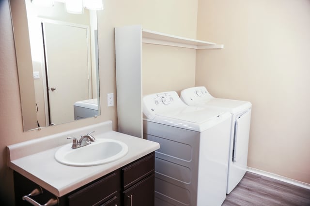 Washer and dryer in apartment laundry area with sink and mirror.