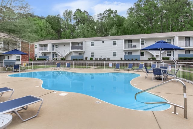 Swimming pool with lounge chairs and tables, adjacent to apartment buildings.