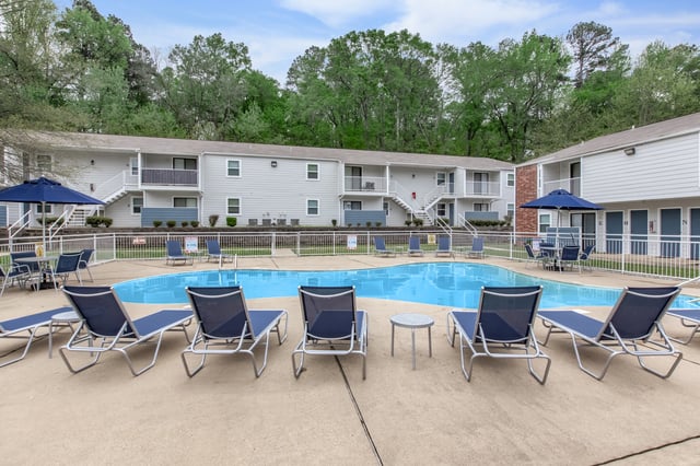 Resort-style swimming pool with lounge chairs and umbrellas, adjacent to apartment buildings.