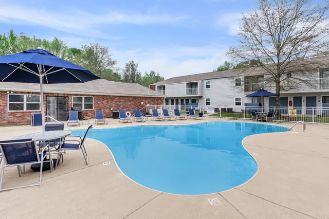 An inviting swimming pool with lounge chairs and umbrellas, next to apartment buildings.