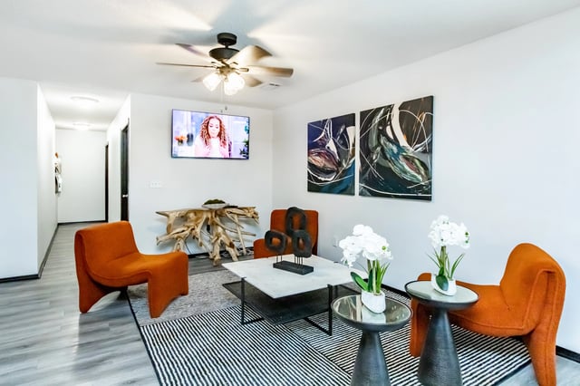 Modern living room with orange accent chairs, a marble coffee table, and abstract art.