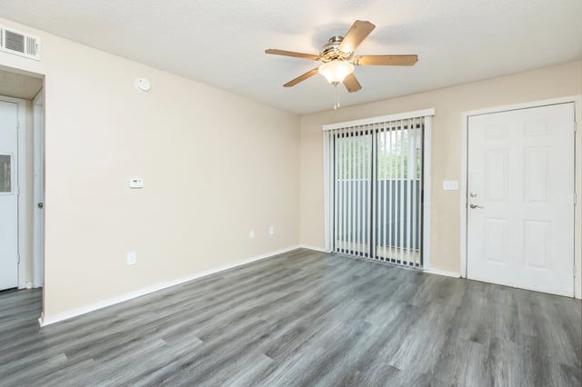 Empty living room with wood laminate flooring, ceiling fan, and sliding glass door.