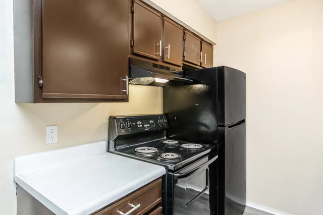 Kitchen with dark brown cabinets, white countertop, and black appliances including a stove and refrigerator.