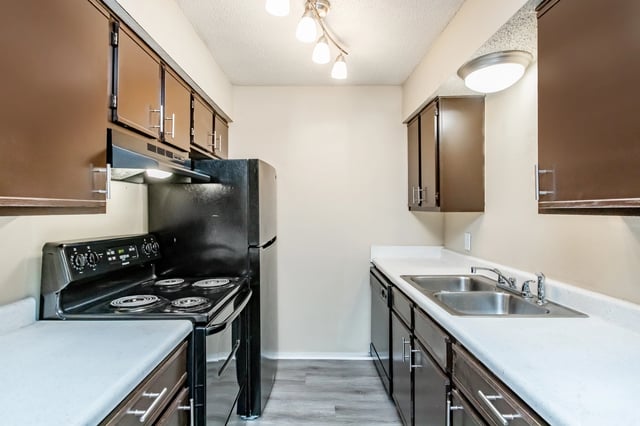 Kitchen with black stove and refrigerator, double sink, and dark brown cabinets.