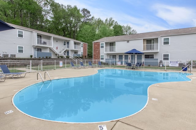 Resort-style swimming pool with lounge chairs and umbrellas, adjacent to apartment buildings.