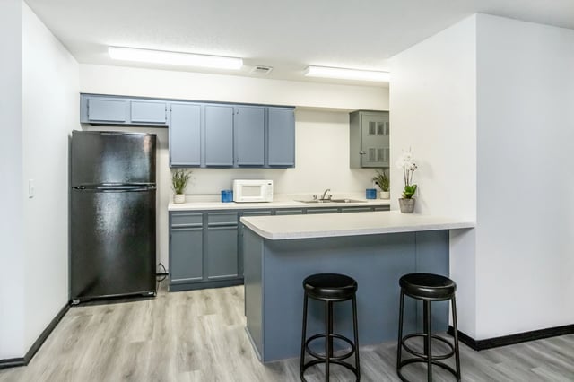 Kitchen area with black refrigerator, gray cabinets, white countertop, microwave, and sink.