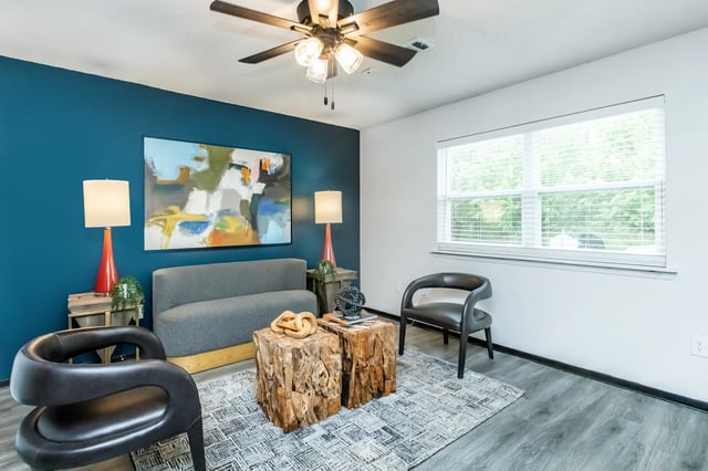 Living room with a teal accent wall, modern furniture, abstract art, and a ceiling fan.
