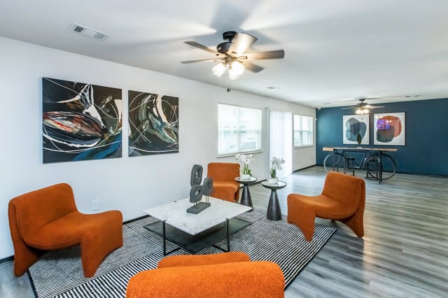 Modern living room with orange chairs, abstract art, and a bicycle-themed table.