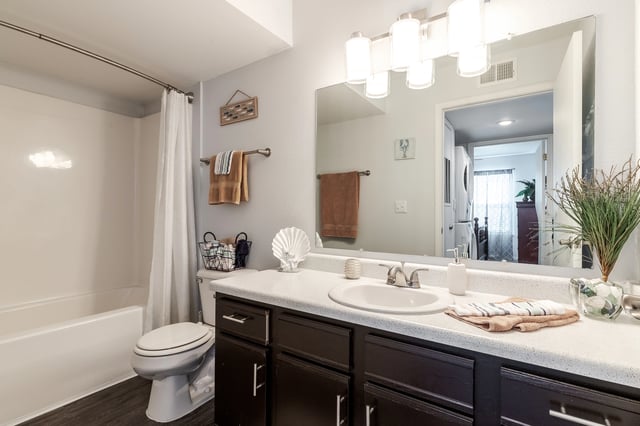 Bathroom vanity with dual sinks and mirrors, bathtub, toilet, and dark wood cabinets.