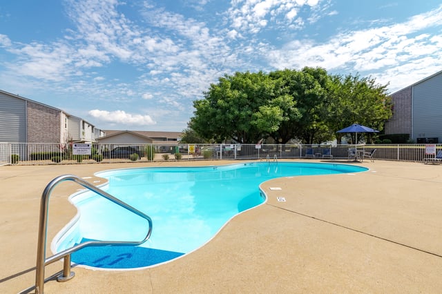 Outdoor swimming pool with lounge chairs and umbrellas under a blue sky with white clouds.