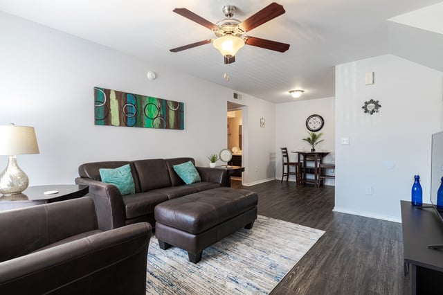 Living room with dark brown sofa, ottoman, and armchair, featuring a ceiling fan and modern art.