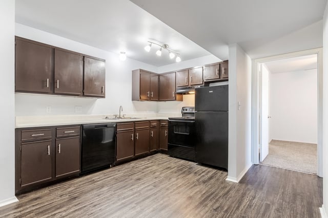 Kitchen with dark brown cabinets, black appliances, and wood-look flooring.