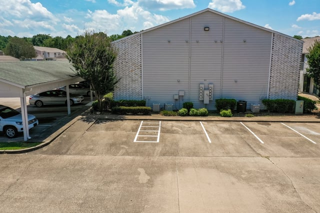 Exterior view of apartment buildings with covered parking and a paved parking lot.