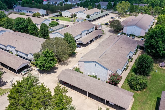 Aerial view of apartment buildings with carports and surrounding trees.