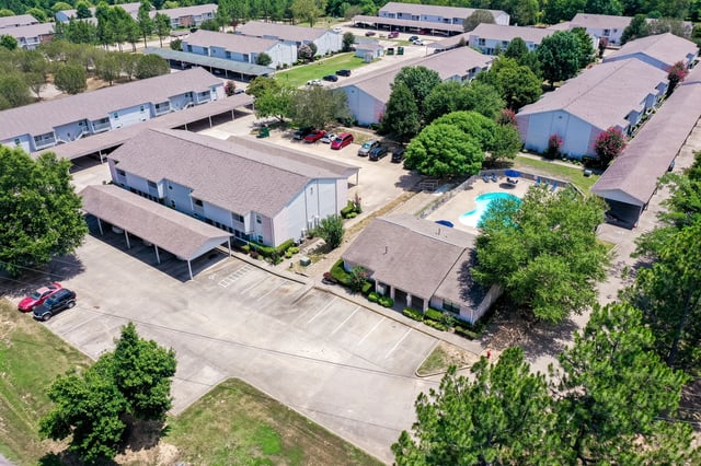 Aerial view of apartment complex with pool, parking, and carports.