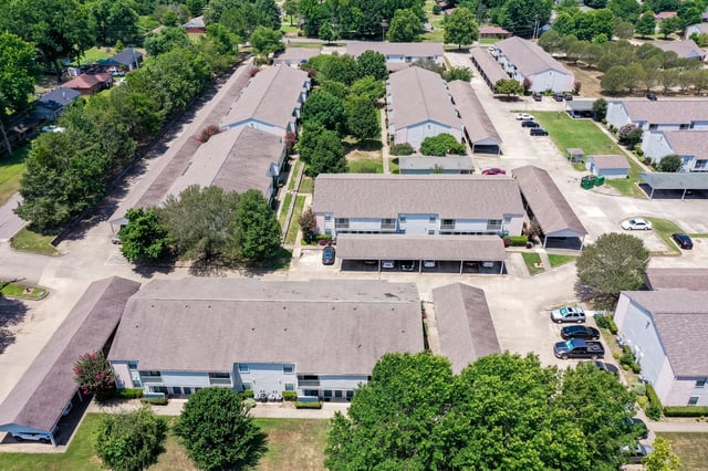 Aerial view of apartment buildings with covered parking and surrounding trees.