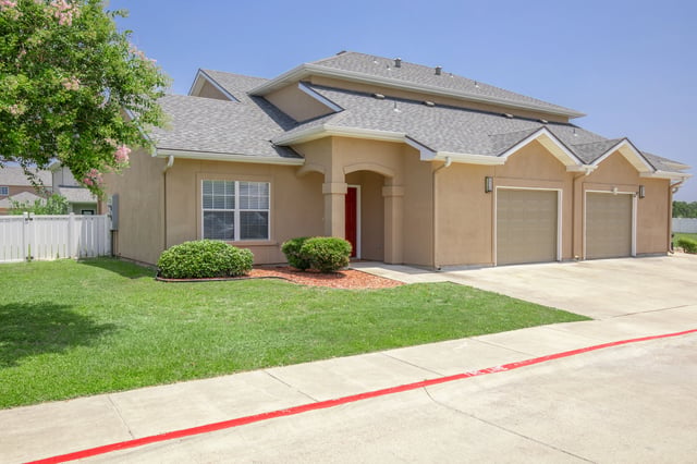 Exterior view of a tan stucco duplex with a red front door and a two-car garage.