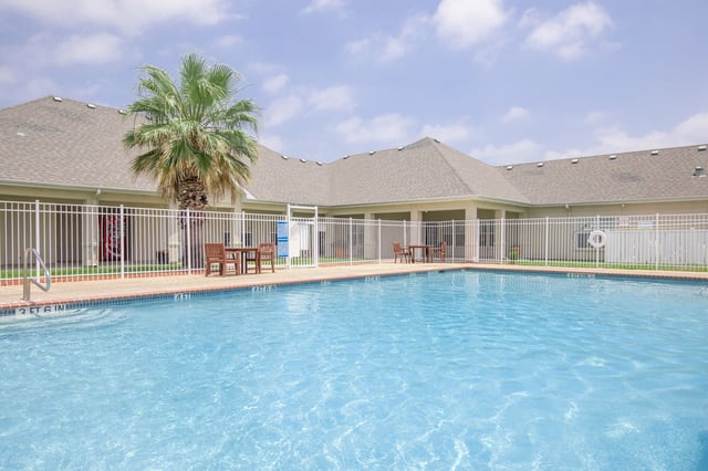 Outdoor swimming pool with lounge chairs and tables, fenced area.