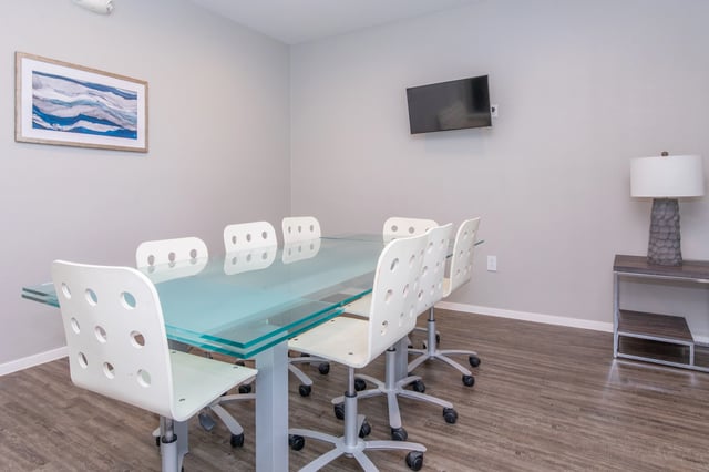 Conference room with a glass table, white chairs, and a wall-mounted TV.