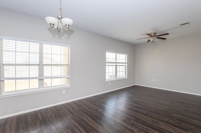 Empty apartment living room with dark wood floors and blinds on windows.