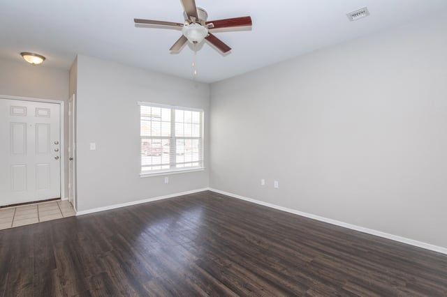 Interior view of an empty apartment living room with a ceiling fan, a window, and a front door.