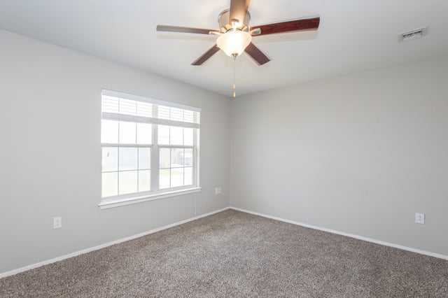 Empty bedroom with a ceiling fan and a large window with blinds.