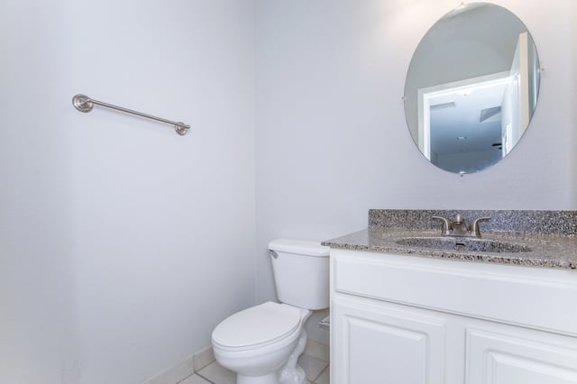 Clean bathroom with a white toilet, vanity with granite countertop, and a round mirror.