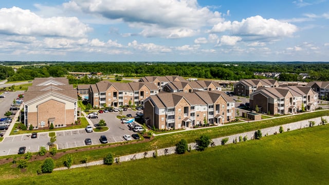 Aerial view of a multifamily apartment complex with brick buildings, manicured lawns, and a swimming pool.