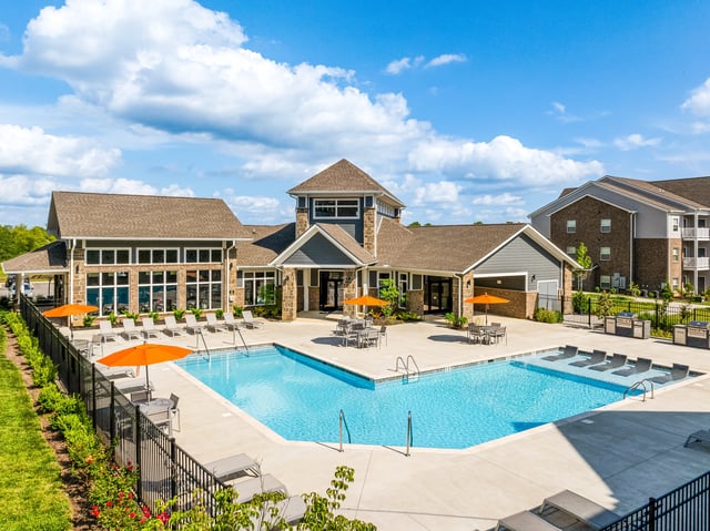 Resort-style swimming pool with lounge chairs, umbrellas, and outdoor grills, adjacent to the property's clubhouse.