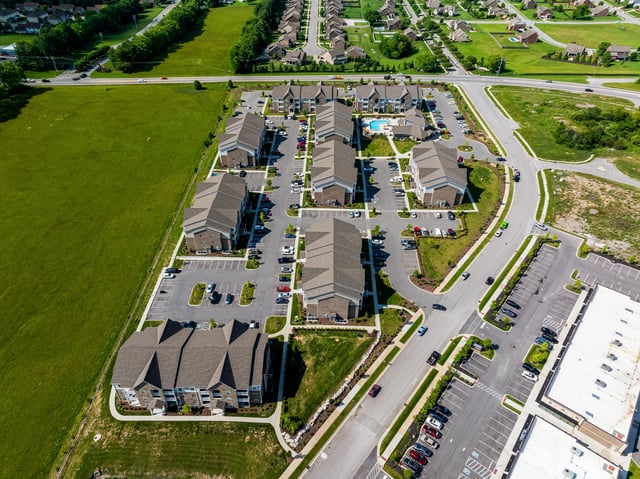 Aerial view of apartment buildings with a pool and surrounding green spaces.