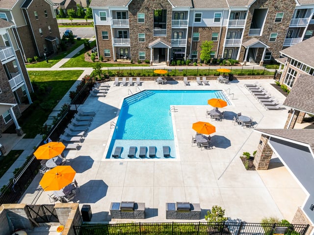 Aerial view of a swimming pool area with lounge chairs, tables with umbrellas, and grills.