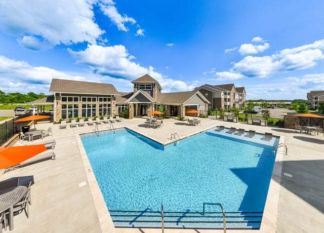 Luxurious swimming pool with lounge chairs and umbrellas, adjacent to apartment buildings.