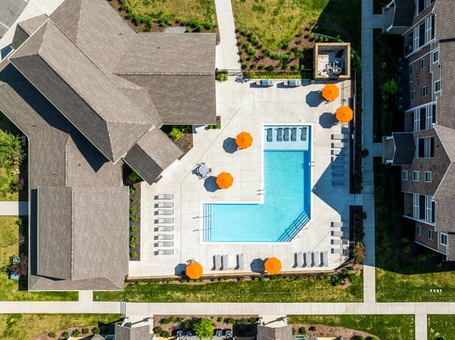 Aerial view of an L-shaped outdoor swimming pool with lounge chairs and orange umbrellas.