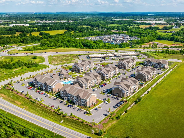 Aerial view of a multifamily property with multiple buildings, a swimming pool, and surrounding landscape.