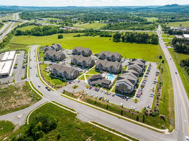 Aerial view of apartment complex buildings, swimming pool, and surrounding landscape.