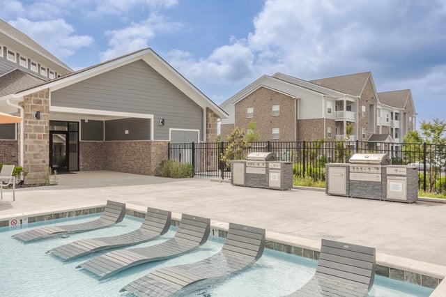 Poolside lounge chairs and outdoor grills at an apartment complex.