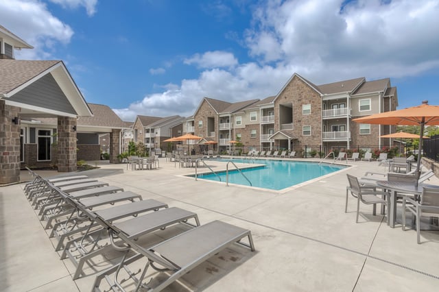 Apartment community pool area with lounge chairs and tables.