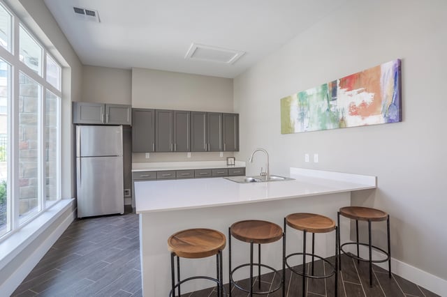 Modern kitchen with stainless steel refrigerator, gray cabinets, and a white island with bar stools.