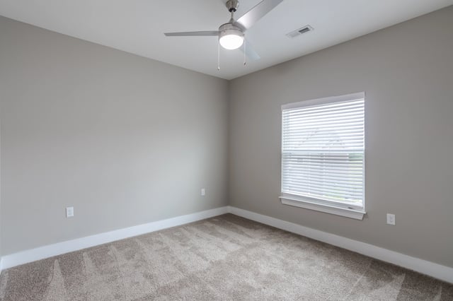 Empty bedroom with beige carpet, neutral walls, a ceiling fan, and a window with blinds.