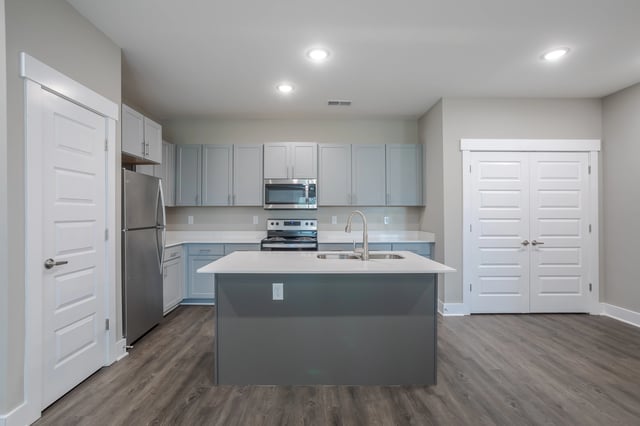 Modern kitchen with stainless steel appliances, gray cabinets, and a large island with a sink.