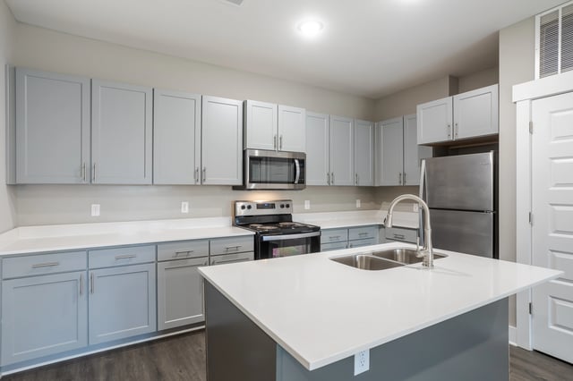 Modern kitchen with light gray cabinets, white quartz countertops, and stainless steel appliances.