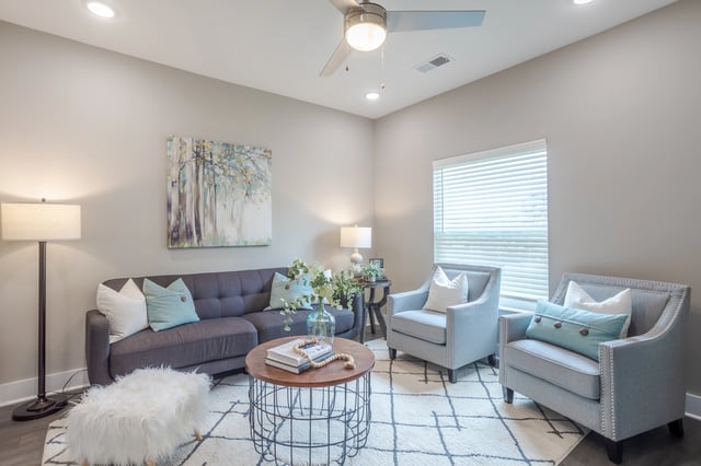 Stylish living room with a gray tufted sofa, two accent chairs, a round coffee table, and a ceiling fan.