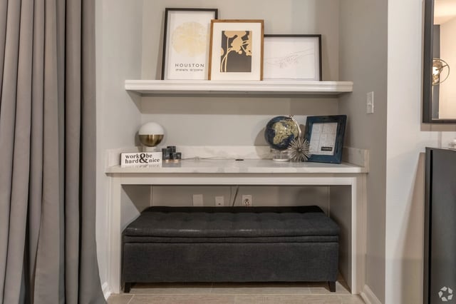 Built-in desk with storage ottoman, featuring artwork and decor.