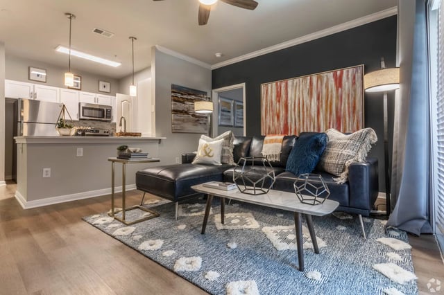 Modern living room and kitchen area with a sectional couch, coffee table, and stainless steel appliances.