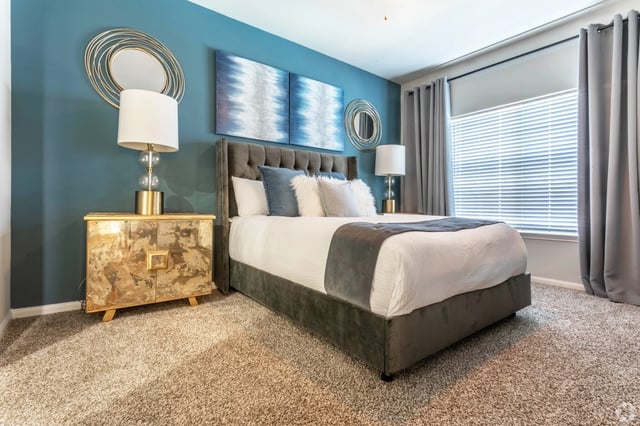 A beautifully decorated bedroom with a large bed, nightstand, and blue accent wall.