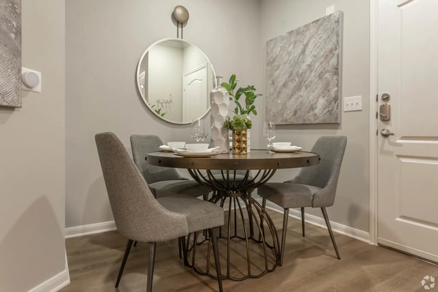 A round dining table with four chairs, set for a meal, near a mirrored wall and a door.