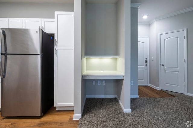 Stainless steel refrigerator next to white cabinets and a built-in desk.