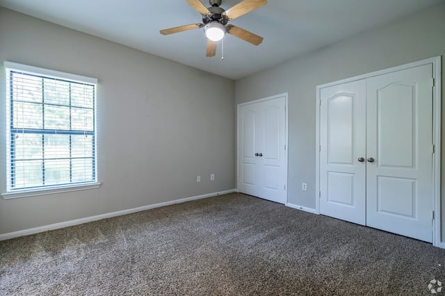 Bedroom with a ceiling fan, a window with blinds, and two closet doors.