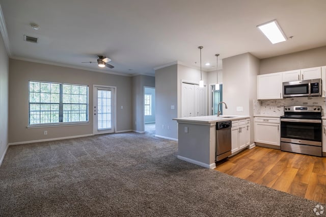 Interior view of a spacious apartment living room and kitchen area with modern appliances and a large window.